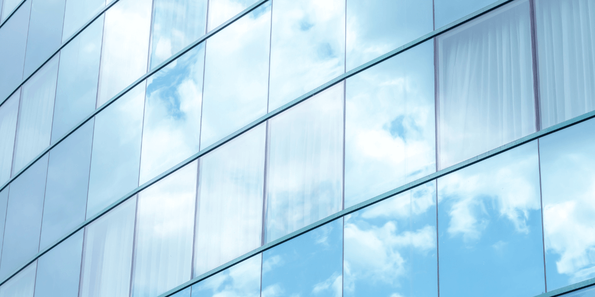 Corporate building with reflective window film mirroring a partially cloudy sky